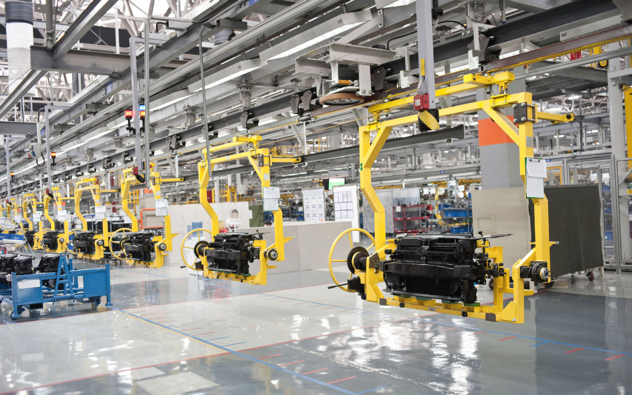 Large factory with a production line of yellow machines and spare part storage in the background.